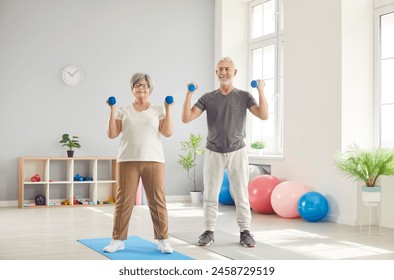 Active happy elderly people, seniors exercising with dumbbells, health care of elderly people, old woman, man lifting weights for morning warming up, caring for physical well-being in sport studio - Powered by Shutterstock