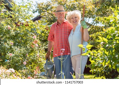 Active happy senior woman looking at camera while standing next to her husband during work in the garden in a sunny day of summer - Powered by Shutterstock