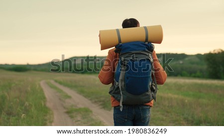Active healthy Caucasian man with a backpack is walking towards a distant mountain. Man hiker hiking in mountains in summer. Traveler travels on a country road, meditation, ecotourism, hiking.