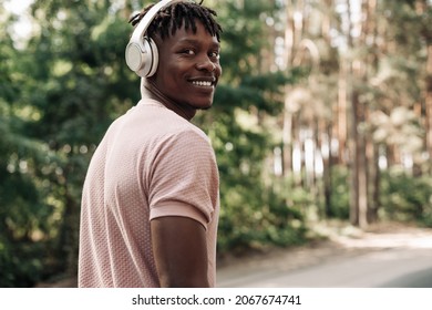 Active healthy happy African American runner, listening to music with headphones, jogging outdoors on the road in the forest, side view of young athletic man running in nature - Powered by Shutterstock
