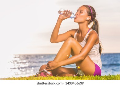 Active healthy lifestyle young woman drinking water bottle wearing true wireless airpods earbuds listening to audiobook or run motivation podcast outdoor on beach. - Powered by Shutterstock