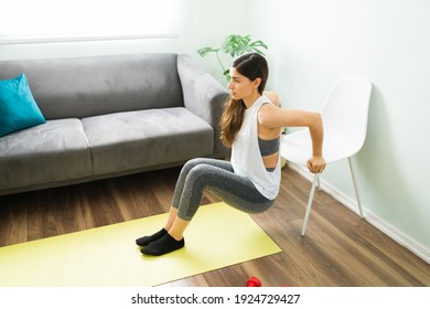 Active and healthy young woman training at home. Beautiful woman in her 20s doing tricep dips with a chair in the living room 