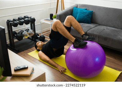 Active hispanic young man using a stability ball for his home workout exercises in the living room - Powered by Shutterstock