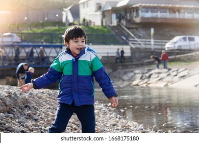 Active Kid Throwing Stone To The Beach Sand With Bright Light On Spring Or Summer, Little Boy Playing With The Rock,Children Exploring By The Seaside, Play And Lean From Nature