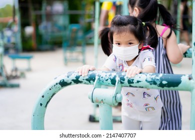 Active Kids Girl Playing Exercise Machine On Publics Park In Summer Time. Cute Child Wearing White Medical Face Mask. Prevent Toxic Dust PM2.5, Air Pollution And Protection Coronavirus. Copy Space. 