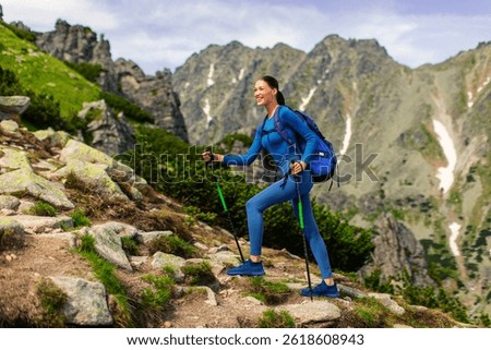 Active lady with backpack using trekking poles and hiking in mountains, enjoying beautiful views, full length shot, side view, free space