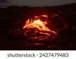 Active lava flow on Hawaii, magma is coming out of a crevice, slowly cooling down and solidifying in various patterns, the glow of the lava is reflected on the black rock all around, Hawaii, Kalapana