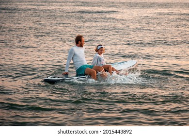 Active leisure. Father and daughter surfing on a sup board and have a funny time. Sea at the background. Family summer vacations.