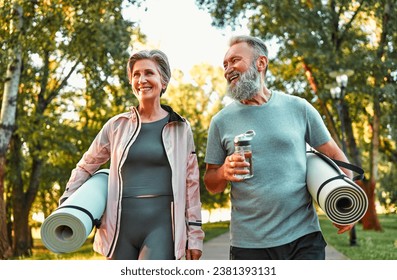 Active life of older people. Happy sports couple going for a workout outdoors, holding exercise mats and water. Health and recovery, healthy living, hobbies in retirement.