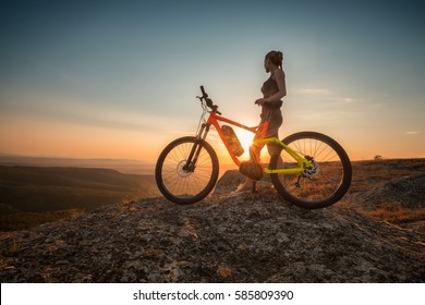 Active life /
A woman with a bike enjoys the view of sunset over an autumn forest - Powered by Shutterstock