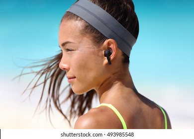 Active life woman listening to music with wireless earbuds. Fitness runner using smartphone phone app on beach wearing earpods on running workout. Asian woman healthy on summer vacation.