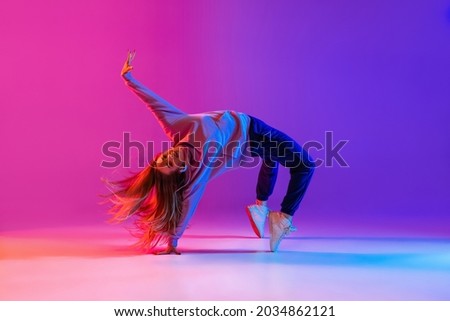 Active lifestyle. Dancing as hobby. Young beautiful female hip-hop dancer expresses emotions in dancing isolated on neon background. Concept of dance, youth, hobby, dynamics, movement, action, ad