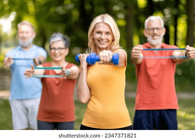 Active Lifestyle. Group of healthy senior people in sportswear training outdoors together, smiling elderly friends exercising with dumbbells and resistance band outside, doing fitness workout in park - Powered by Shutterstock