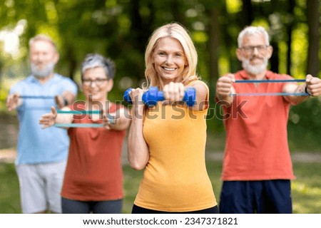Active Lifestyle. Group of healthy senior people in sportswear training outdoors together, smiling elderly friends exercising with dumbbells and resistance band outside, doing fitness workout in park