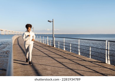 Active Lifestyle. Happy Young African American Woman In Sportswear Jogging Outdoors, Athletic Black Millennial Lady Running On Wooden Pier Near Sea, Enjoying Training Outside, Copy Space