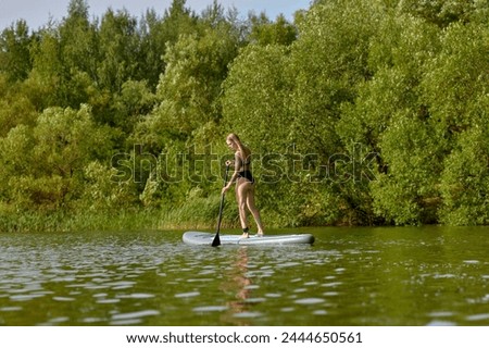 An active lifestyle personified: a sunlit image showcasing a determined woman practicing stand-up paddleboarding with skill