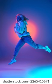 Active lifestyle  plans  Young woman in casual clothes  hoodie   jeans running over gradient studio background in blue neon light  Concept emotions  facial expression  inspiration  sales  ad