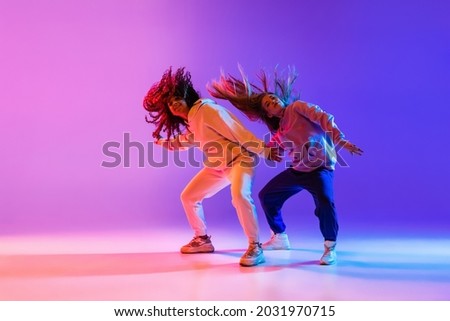 Active lifestyle. Two beautiful hip-hop dancers in motion on gradient pink purple neon background. Sport achievement, expression. Concept of dance, youth, hobby, dynamics, movement, action, ad