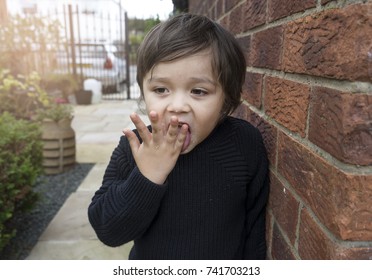 Active little boy hiding next to wall brick and licking his fingers after finished eating sweet cotton candy, Unhealthy food concept
