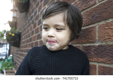Active little boy hiding next to wall brick and licking his fingers after finished eating sweet cotton candy, Unhealthy food concept