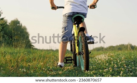 Active little boy rides fast bicycle across grassy field in summer evening