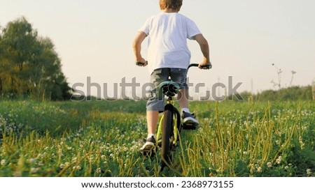 Active little boy rides fast bicycle across grassy field in summer evening