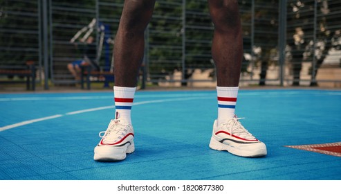 Active male basketball player practicing ball handling skill, dribbling ball between legs on outdoor court. Close up of African American man legs in white socks training cross bouncing with ball - Powered by Shutterstock