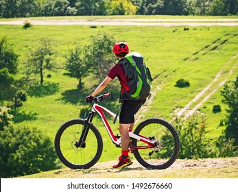 Active man with backpack riding full suspension bicycle on trail at natural background