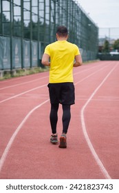 Active man in comfortable activewear jogs along the stadium track, healthy and active lifestyle backside view. 