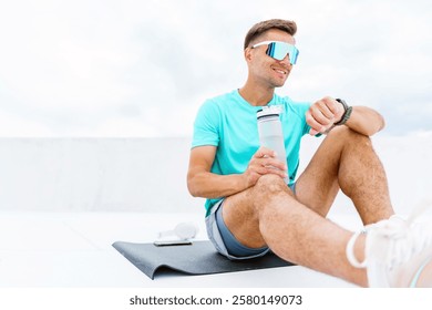 Active man enjoying a break while checking watch after workout on rooftop in daylight