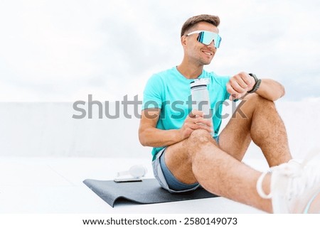 Active man enjoying a break while checking watch after workout on rooftop in daylight