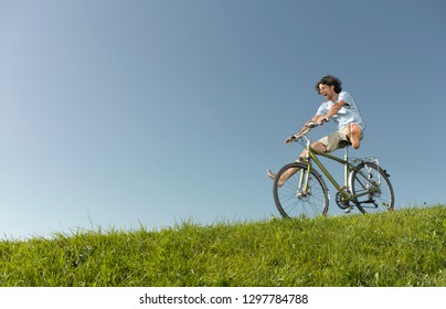 Active man freewheeling down grassy hill on a bike in summertime