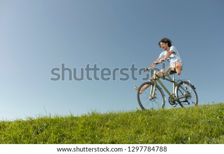 Active man freewheeling down grassy hill on a bike in summertime