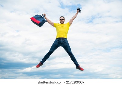 Active man jumping with travel bag midair sky background, vacation