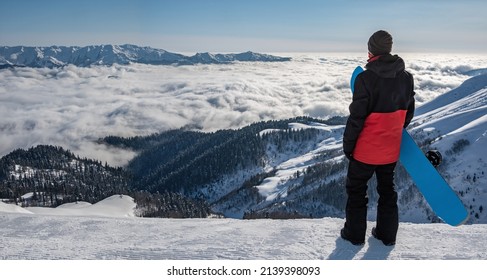 Active man with snowboard looking at mountains in clouds at sunset