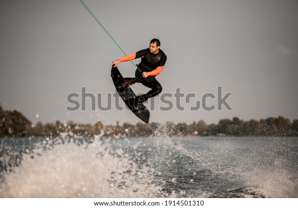 active man in wetsuit having\
fun and masterfully jumping on the wave on wakeboard. Active\
leisure