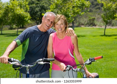 Active Mature Couple Exercise By Riding Bikes In Park At Camera