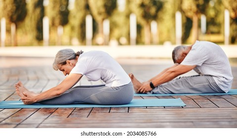 Active mature family man and woman doing yoga exercise seated forward bend while exercising in morning on fresh air, stretching back over legs, senior couple practicing Paschimottanasana