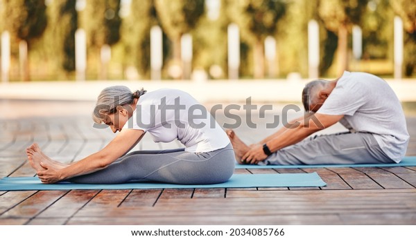 Active\
mature family man and woman doing yoga exercise seated forward bend\
while exercising in morning on fresh air, stretching back over\
legs, senior couple practicing\
Paschimottanasana