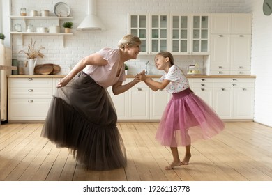 Active mature grandma dance with small granddaughter on warm floor at modern kitchen in puffy ballerina skirts. Joyful senior nanny play princesses with little girl dancing listen to music having fun - Powered by Shutterstock