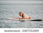 Active mature male paddler with his paddleboard and paddle on a sea at summer. Happy senior man stands with a SUP board. Stand up paddle boarding - outdor active recreation in nature.