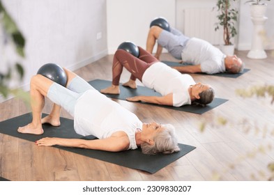 Active mature woman doing exercises with pilates ball during group training at gym indoor - Powered by Shutterstock