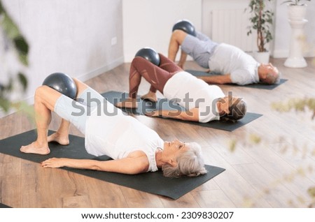 Active mature woman doing exercises with pilates ball during group training at gym indoor