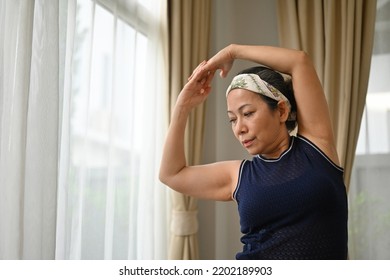 Active Mature Woman Doing Stretching Exercise In Living Room At Home. Fit Lady Stretching Arms And Back.