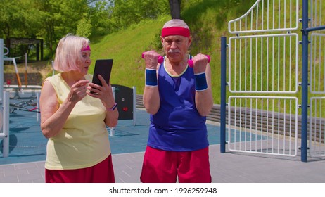 Active mature woman grandmother coach trainer using digital tablet and teaching grandfather with sport weightlifting fitness aerobics dumbbells exercises on playground. Technologies for senior people - Powered by Shutterstock