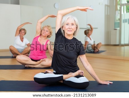 Active mature woman performing stretching between asanas during group yoga training at gym. Fitness and Hatha yoga concept.