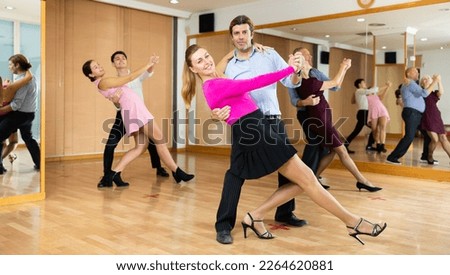 Active middle-aged pair practicing ballroom dance in training hall during dancing-classes. Pairs training ballroom dance