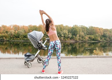 active mother is engaged in sports on the embankment of the river together with the child in a baby carriage. sports mom looks at her baby in a baby carriage and performs tilts towards the body