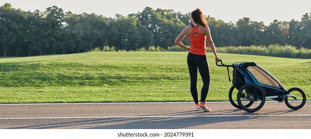 Active mother in sportswear uses jogging stroller for running at park. Happy woman having fun while workout outdoor. Jogging stroller advertisement