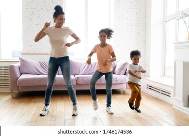 Active Mother Teaches Little Children Son And Daughter To Dance, Lively African Ethnicity Family Fooling Around Moving Enjoy Weekend Having Fun Together In Modern Living Room At Home, Full Length View